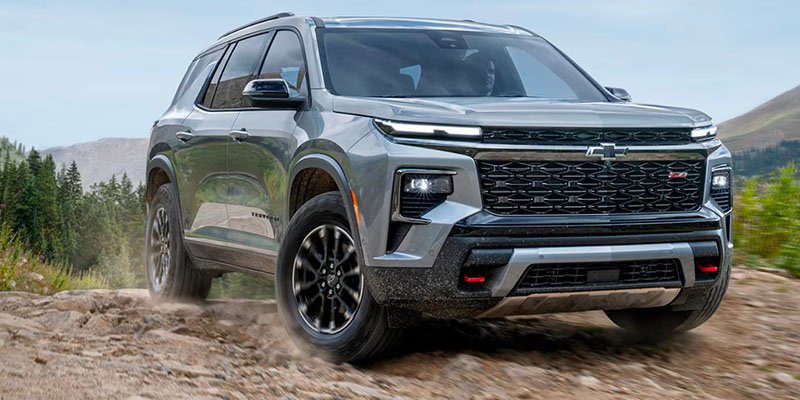 2025 Chevrolet Traverse SUV driving off-road on a rocky mountain trail, showcasing its rugged design, bold front grille, and advanced all-terrain performance.